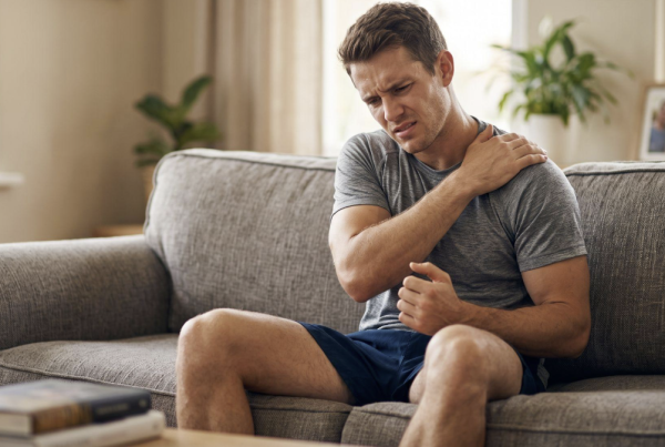 Man sitting in his living room grabbing his painful shoulder, illustrating the need for chiropractic pain relief.